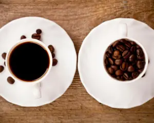 A freshly brewed cup of coffee placed beside a small pile of roasted coffee beans, highlighting the rich ingredients used to create a flavourful and aromatic coffee.