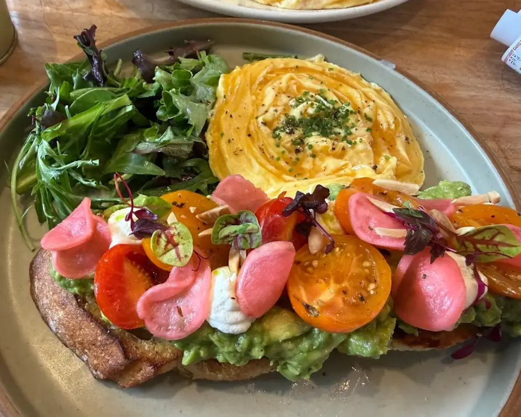 A beautifully plated breakfast dish with perfectly cooked eggs, thick-cut maple-glazed bacon, and a fresh mesclun salad, offering a balanced mix of savoury richness and crisp, refreshing greens.