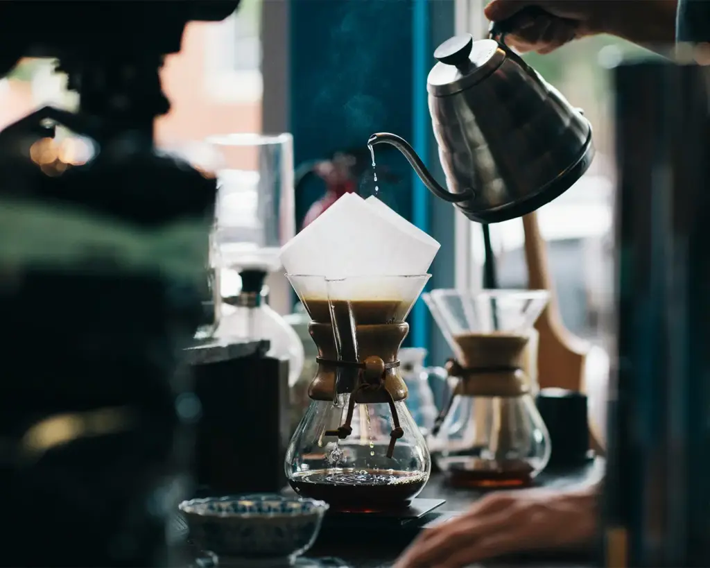 A barista carefully pouring hot water into a cup of coffee during the brewing process, capturing the craft and precision behind making a freshly prepared cup.