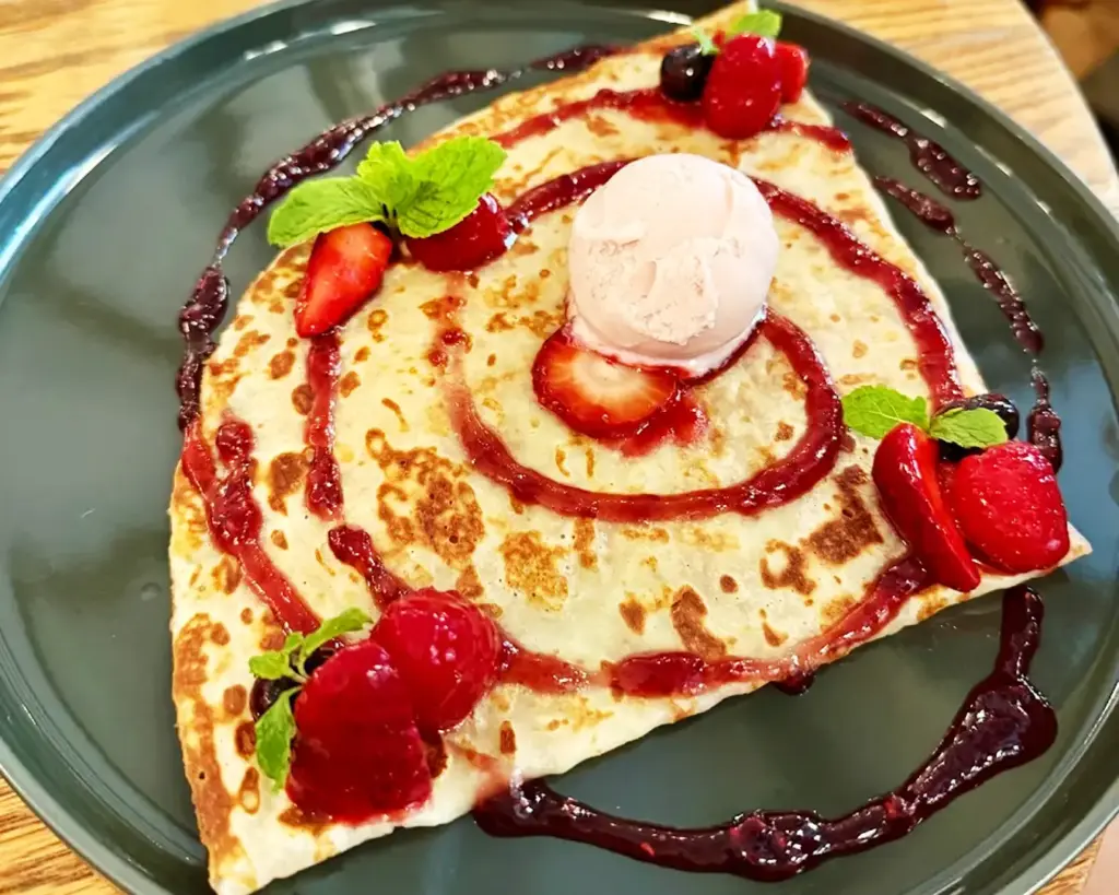 A delicate sweet crêpe topped with fresh strawberries and sauce, folded elegantly on a plate, highlighting a classic French dessert with a bright and appetising presentation.