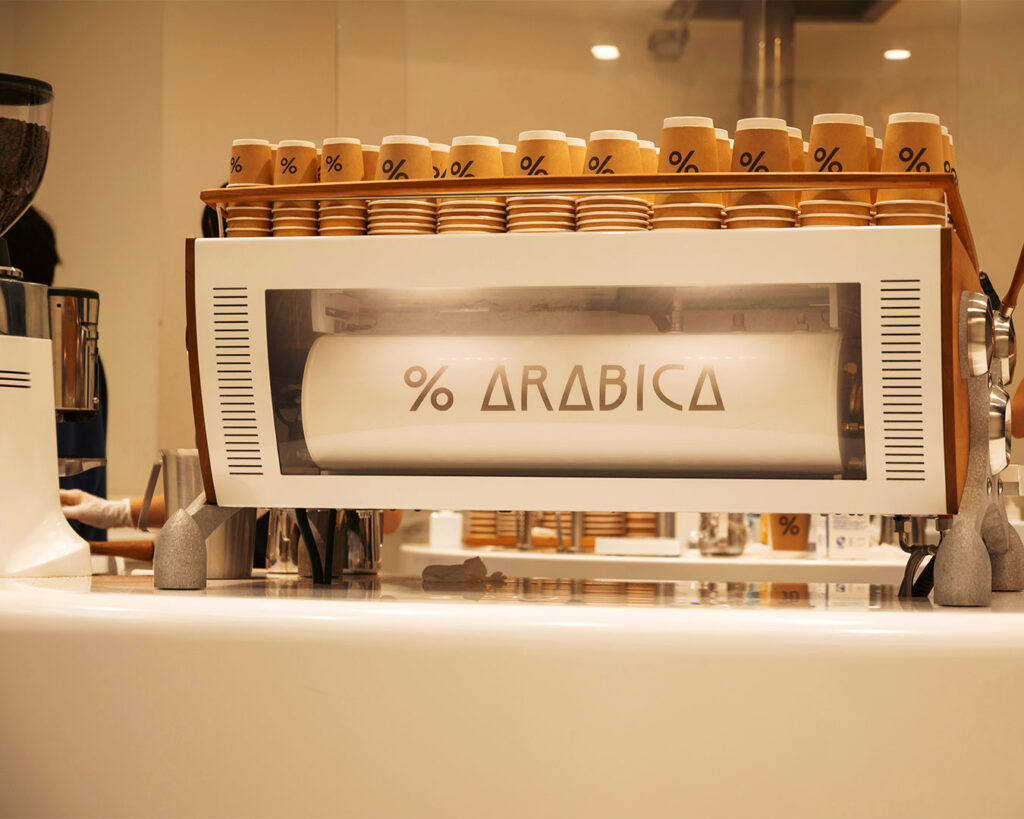 The minimalist interior of an Arabica coffee café, showcasing sleek counters, brewing equipment, and customers enjoying their drinks in a calm, stylish setting.