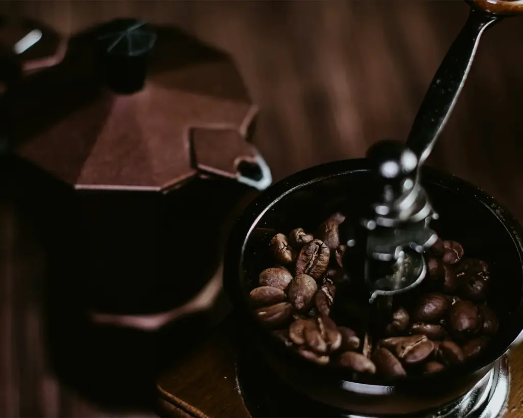 Whole coffee beans being poured into a coffee grinder, ready to be ground into fine coffee powder for brewing fresh coffee.