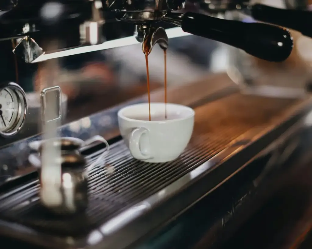 An espresso machine extracting a fresh shot of coffee as dark espresso slowly drips into a cup beneath the portafilter.
