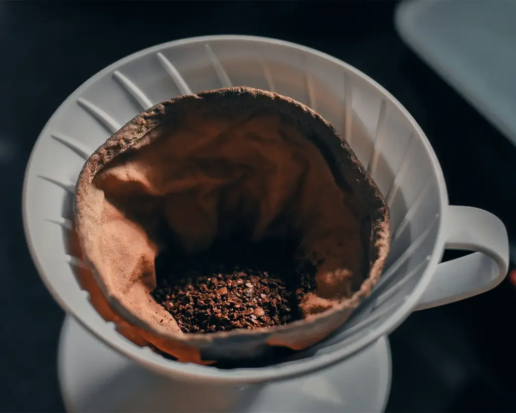 Ground coffee resting evenly in a strainer or filter, prepared for brewing, illustrating the step where water will pass through to extract the coffee’s essence.