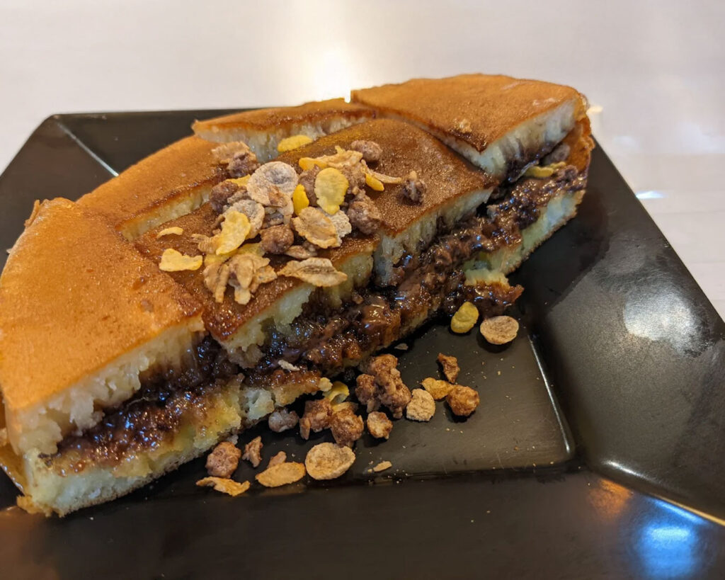 A freshly cooked martabak pancake cut into slices, showing its soft, fluffy texture and rich filling, served on a plate with a slightly golden surface.