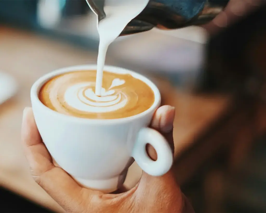 Creamy milk being gently poured into a cup of dark coffee, creating a smooth swirl and soft contrast, capturing a calming moment of blending flavours into a comforting drink.