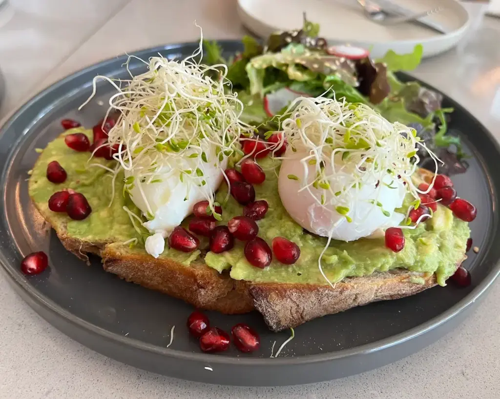A plated breakfast of golden toasted bread served with soft boiled eggs and creamy avocado spread, styled as a simple yet wholesome brunch dish.