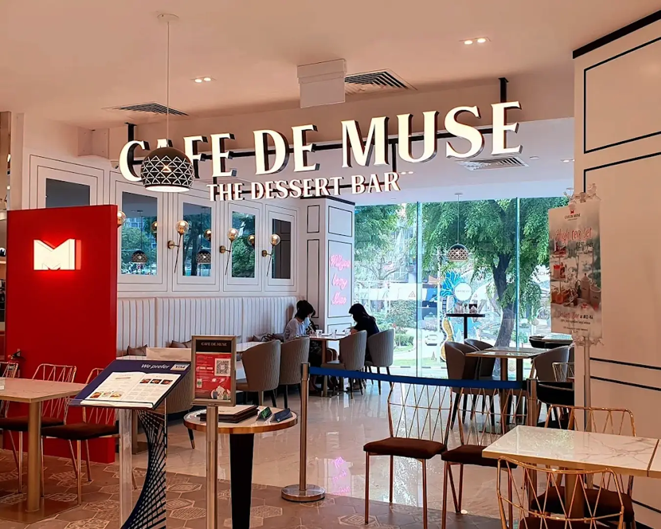 Interior of "Cafe de Muse," a dessert bar with cozy seating. Customers are seated near large windows, creating a bright, inviting atmosphere.