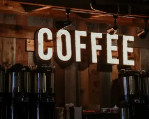 Illuminated "COFFEE" sign on a rustic wooden wall, with several coffee dispensers below, creating a warm and inviting café ambiance.