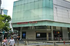 Exterior view of the Orchard Plaza building, with large glass windows reflecting trees, and patrons walking around outside in Singapore, a destination with a calm, urban setting featuring various cafes and nearby coffee spots.