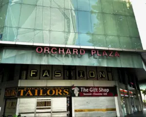 Exterior of Orchard Plaza with large glass windows reflecting trees. Calm, urban setting.