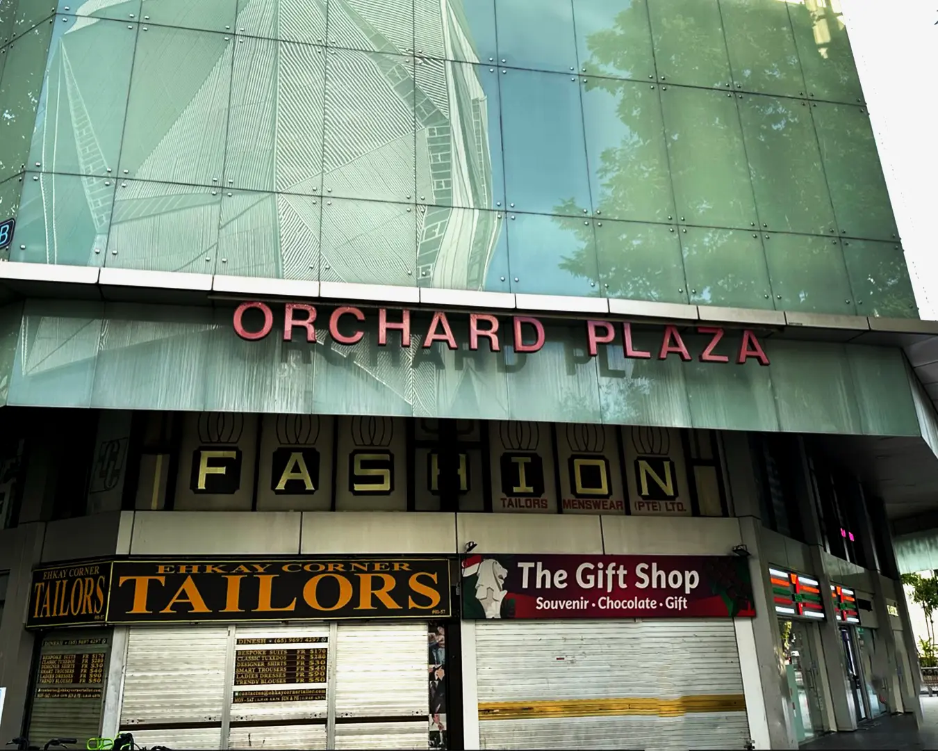 Exterior of Orchard Plaza with large glass windows reflecting trees. Calm, urban setting.