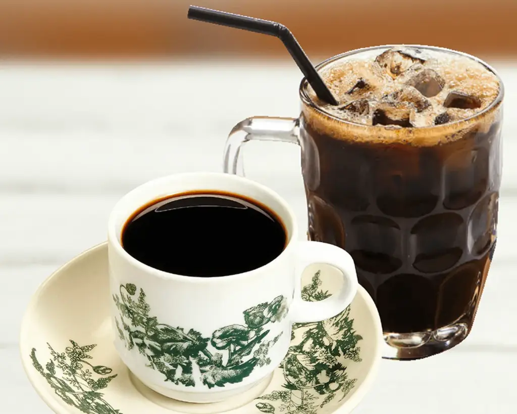 A cup of black coffee in a white ceramic cup with green floral designs sits on a saucer. Beside it is an iced coffee in a glass mug with a straw.