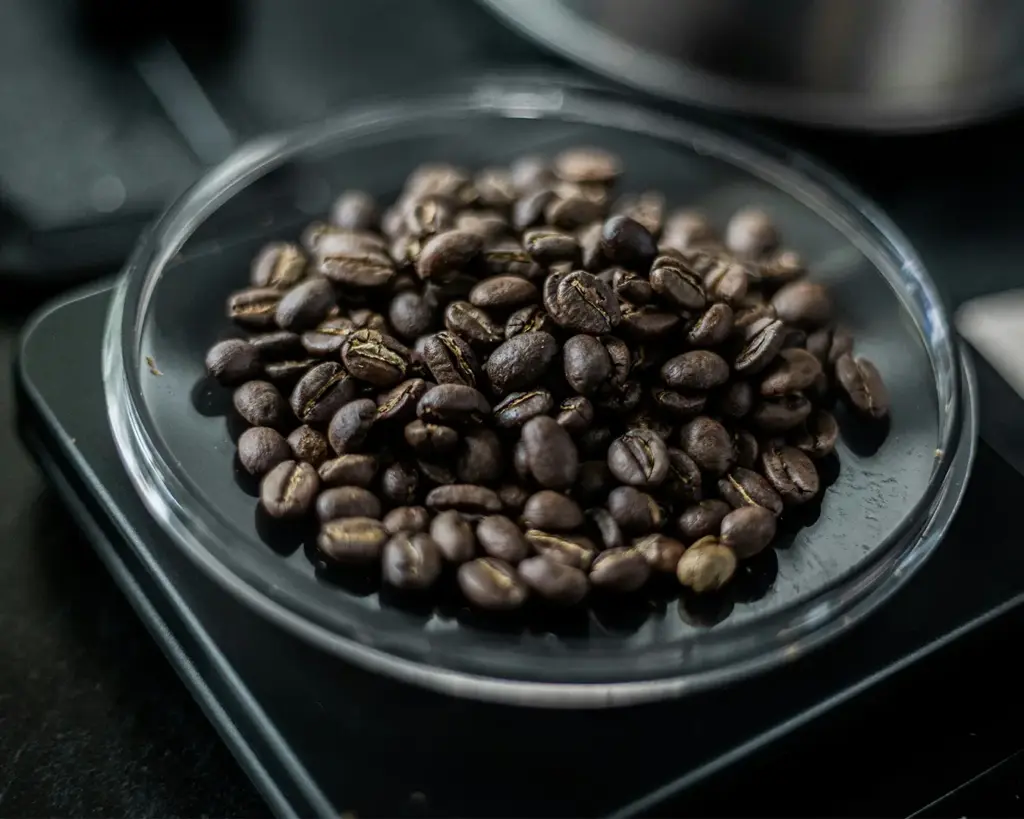 Close-up of dark roasted coffee beans in a clear glass dish on a black surface.