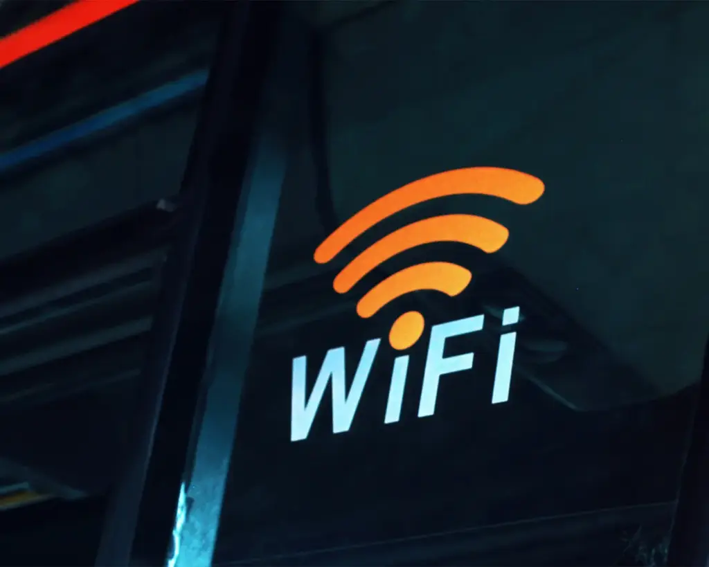 Orange WiFi symbol and text on a dark bus window, indicating internet availability. The warm glow suggests connectivity and accessibility.