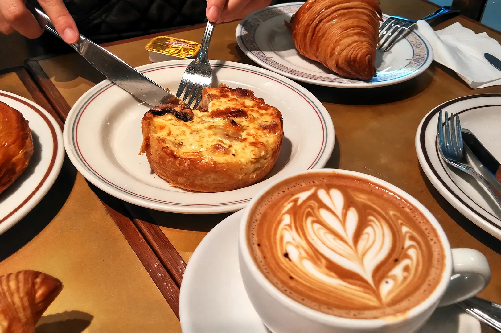 A close-up of a delicious brunch spread featuring a savory quiche, buttery croissant, and a latte with intricate latte art, highlighting comforting and lively cafe culture in Somerset.