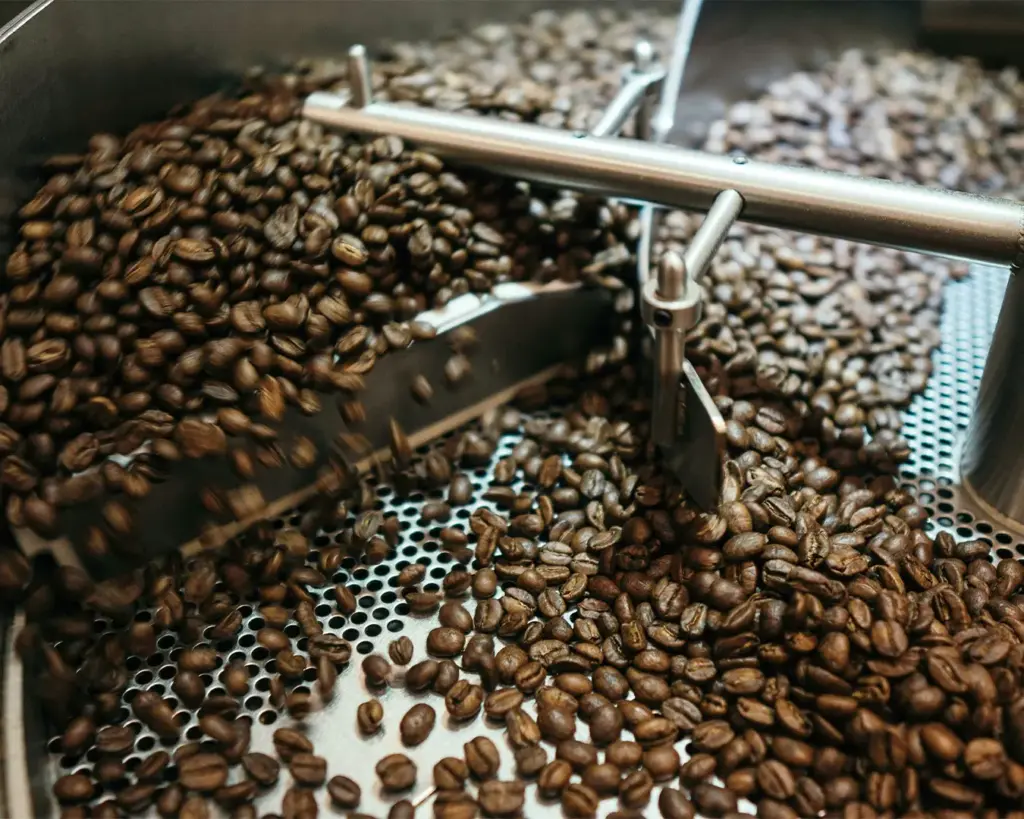 Freshly roasted coffee beans being churned in a large metal roasting machine, creating a rich and aromatic ambiance with a sense of warmth.