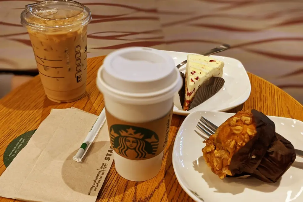A relaxing table setting at Starbucks in Somerset, featuring an iced coffee, a hot beverage, a slice of cheesecake, and a freshly baked muffin to savour for a perfect afternoon break.