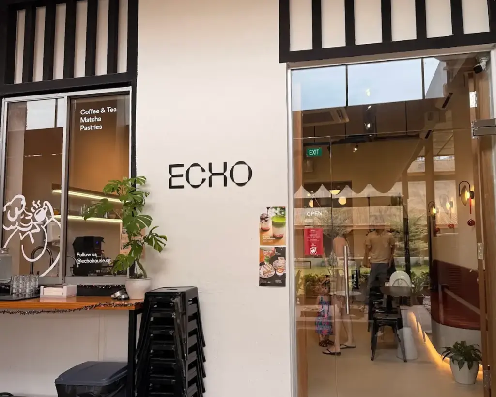Café entrance with "ECHO" on the wall. Glass door reveals a cozy interior. Menu options for coffee, tea, and pastries displayed. Stacked chairs nearby.
