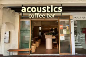 Exterior view of Acoustics Coffee Bar on Neil Road, featuring a minimalist storefront, warm wooden accents, and a clear "acoustics coffee bar" signage.