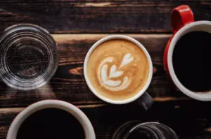 Top-down view of a cup of latte art coffee alongside black coffee and glasses of water on a rustic wooden table, representing Singaporean coffee culture.