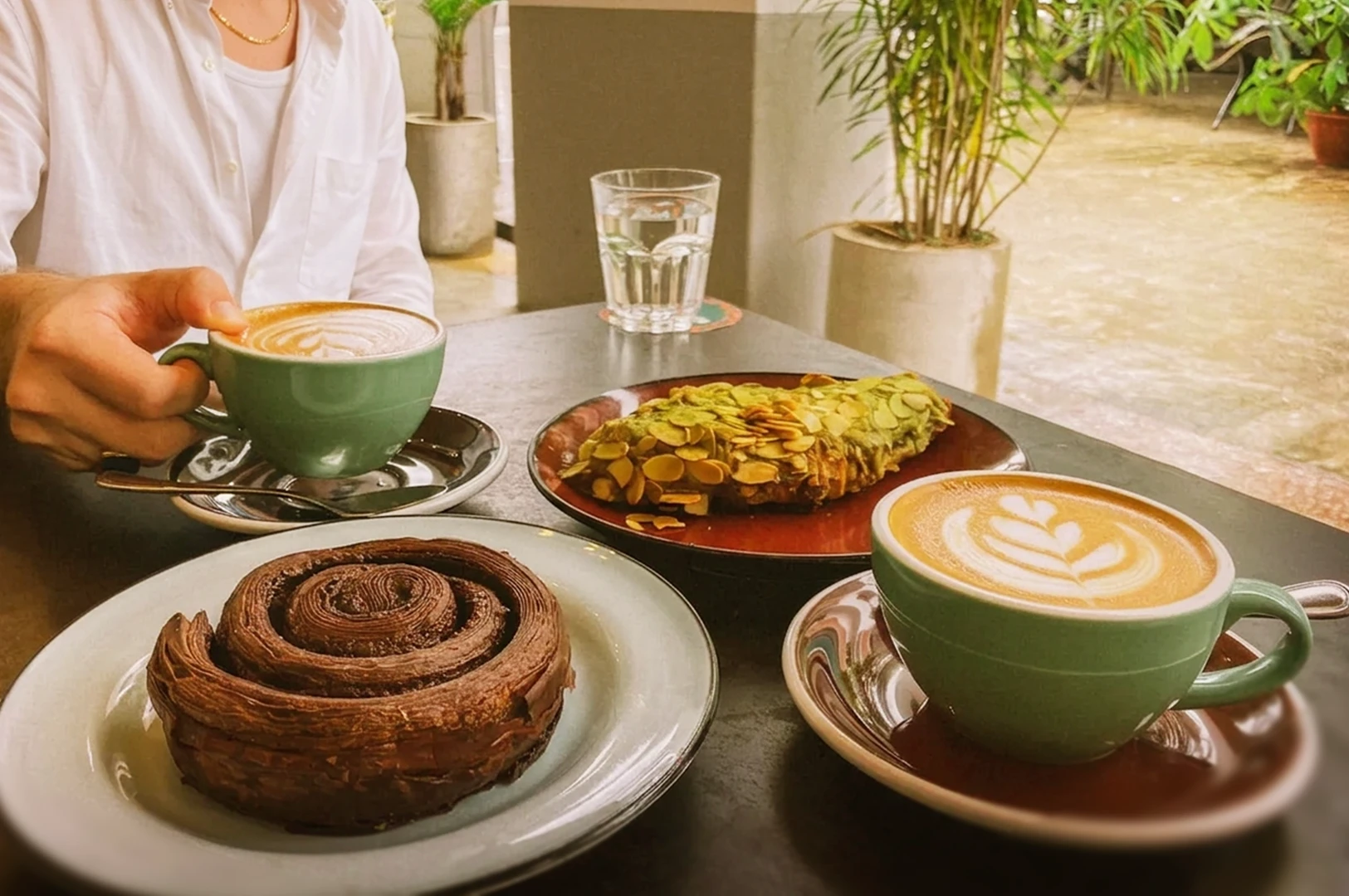 A remote worker enjoying a productive break with coffee and pastries at the outdoor seating of a café, highlighting the inviting atmosphere and peaceful place of Singapore's popular work-friendly café culture.
