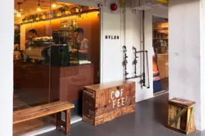 The exterior entrance of Nylon Coffee Roasters in Everton Park, Singapore, featuring a cozy wooden bench and a minimalist shopfront with a warm, inviting atmosphere.