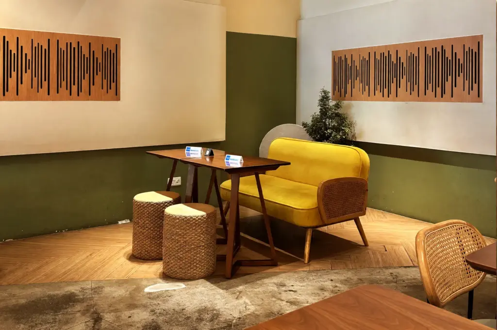 Cozy interior seating area at Acoustics Coffee Bar with a bright yellow sofa, wooden table, and unique sound wave wall art decor.