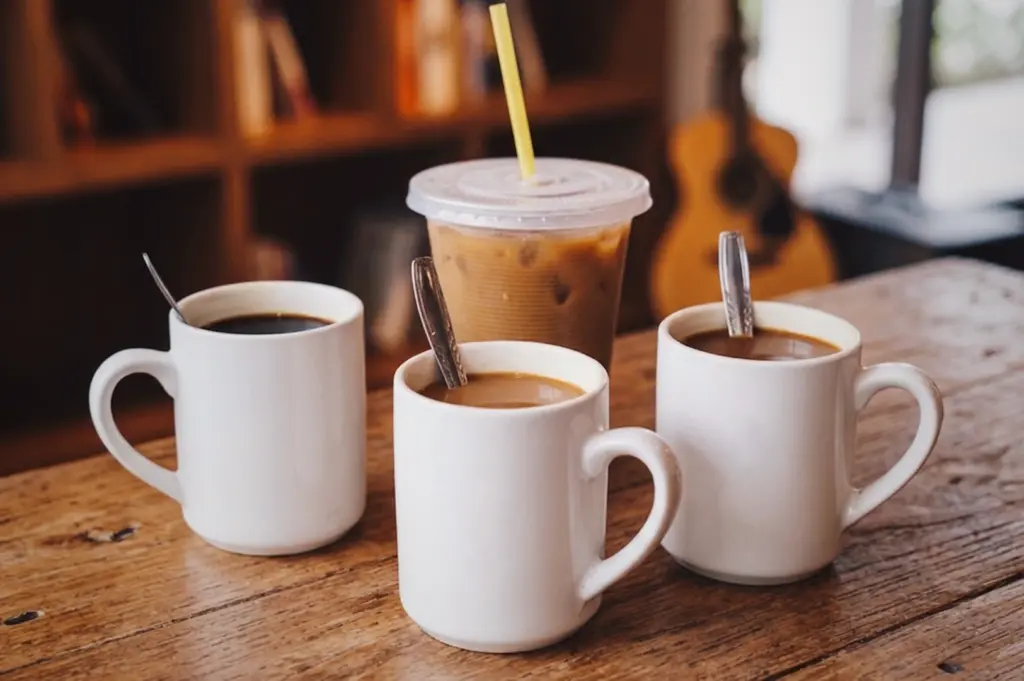 A selection of authentic Singaporean coffee, featuring hot mugs of classic Kopi, Kopi-o, kopi-c, and an iced Kopi with a straw, served on a wooden table.