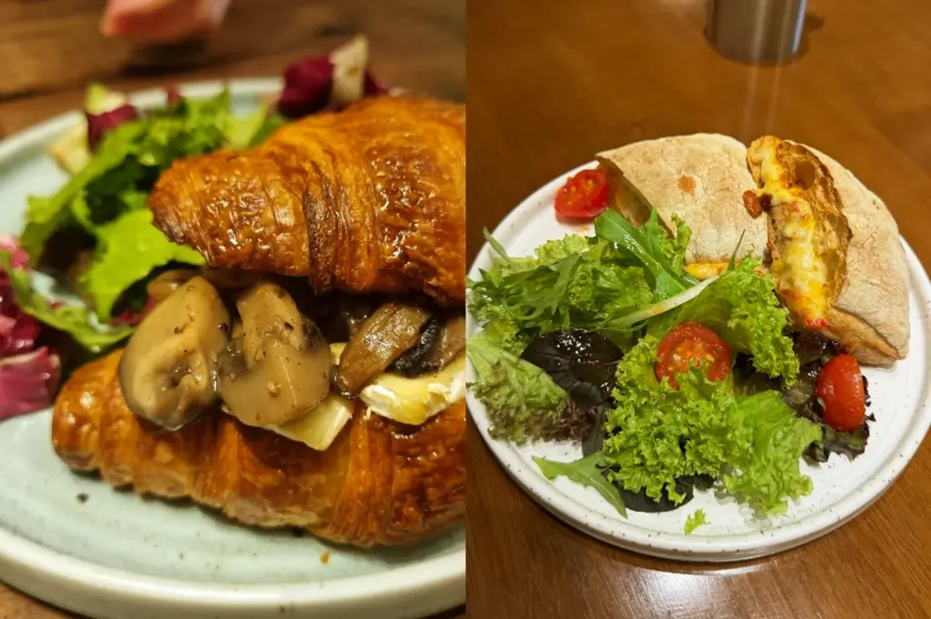 A delicious brunch spread at Acoustics Coffee Bar, featuring a mushroom croissant sandwich and a roasted chicken pita pouch with cherry tomatoes topped on a bed of side salad.