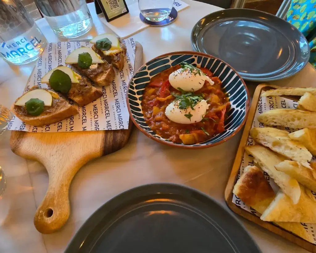 A table set with plates of toasted bread, poached eggs on a tomato-based dish, and water glasses at a restaurant.