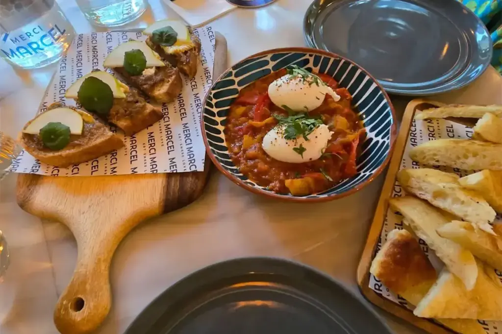 A table set with plates of toasted bread, poached eggs on a tomato-based dish, and water glasses at a restaurant.