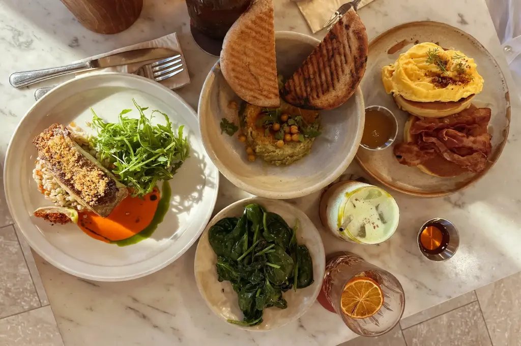 Top-down view of a variety of tea and brunch mains influenced from asia, including pancakes, toasted bread, and side salads, on a marble table at Common Man Coffee Roasters in Joo Chiat Road.