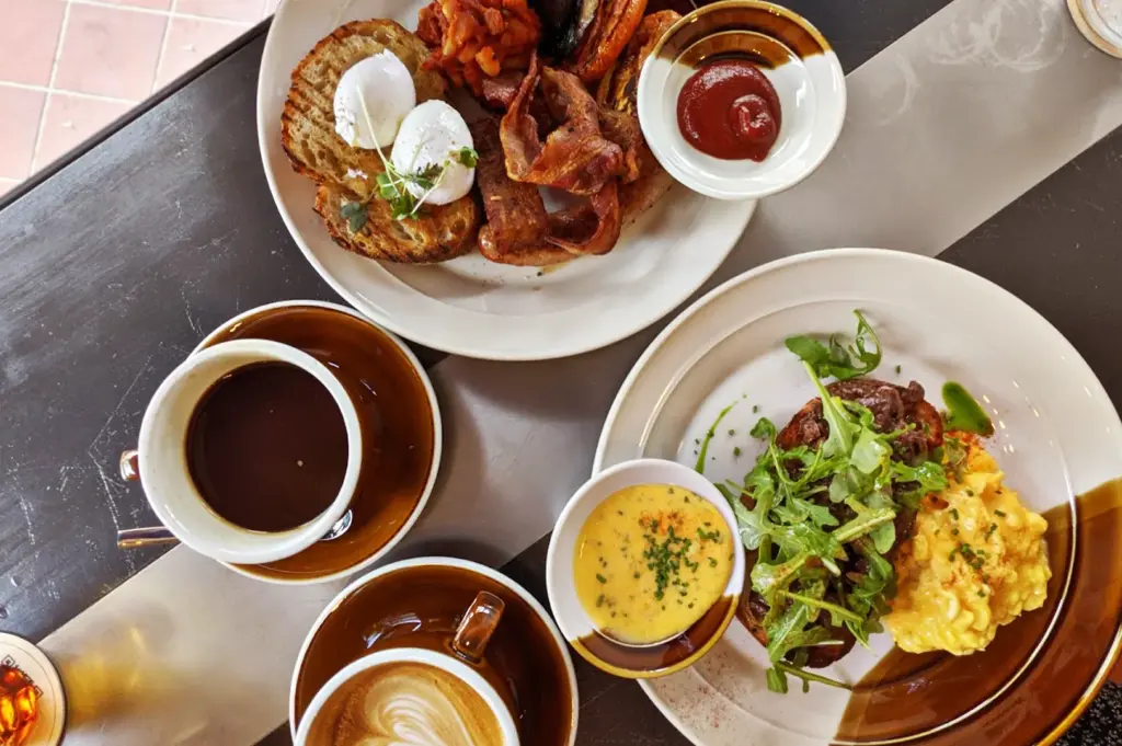 Full breakfast spread at Common Man Coffee Roasters in Joo Chiat, featuring eggs, bacon, and freshly brewed coffee in a rustic café setting.