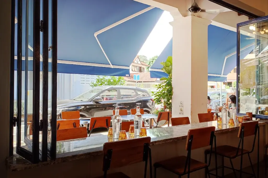 The outdoor seating area at Common Man Coffee Roasters in Joo Chiat, featuring bar-style counter seating under large blue awnings, for the means of comfort outdoors, with views of the street.