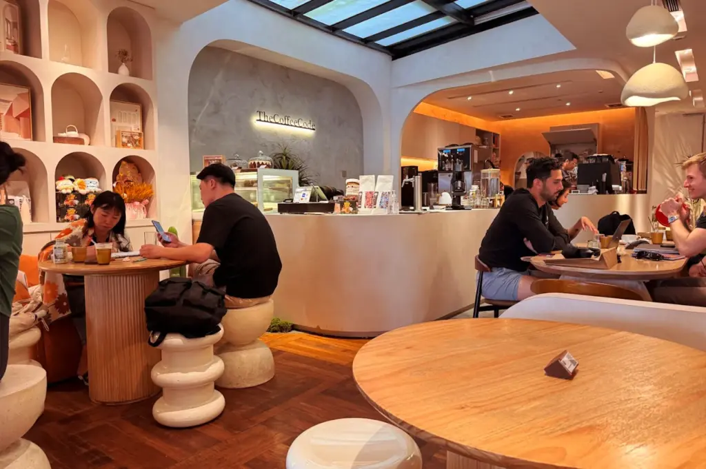 A relaxed atmosphere at The Coffee Code Singapore with patrons working and chatting at round wooden tables, highlighting the cafe's spacious and bright interior.