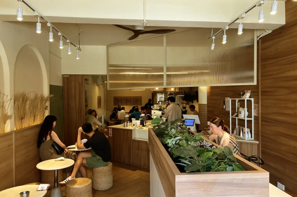 Inside the inviting ambiance of Acoustics Coffee Bar on Neil Road, showing patrons seated in a calm, modern space with wooden furniture and lush indoor greenery.