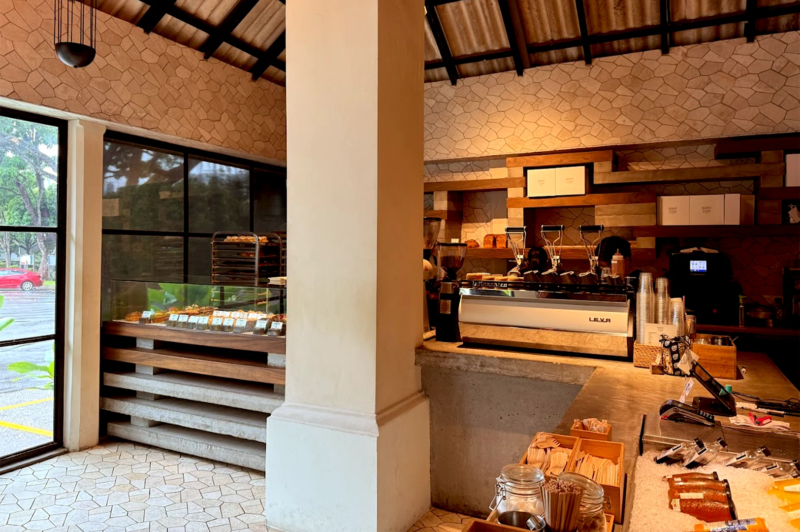 Interior view of Burnt Ends Bakery in Singapore, featuring a modern service counter with a professional espresso machine, display cases filled with artisan pastries, and a rustic tiled wall.