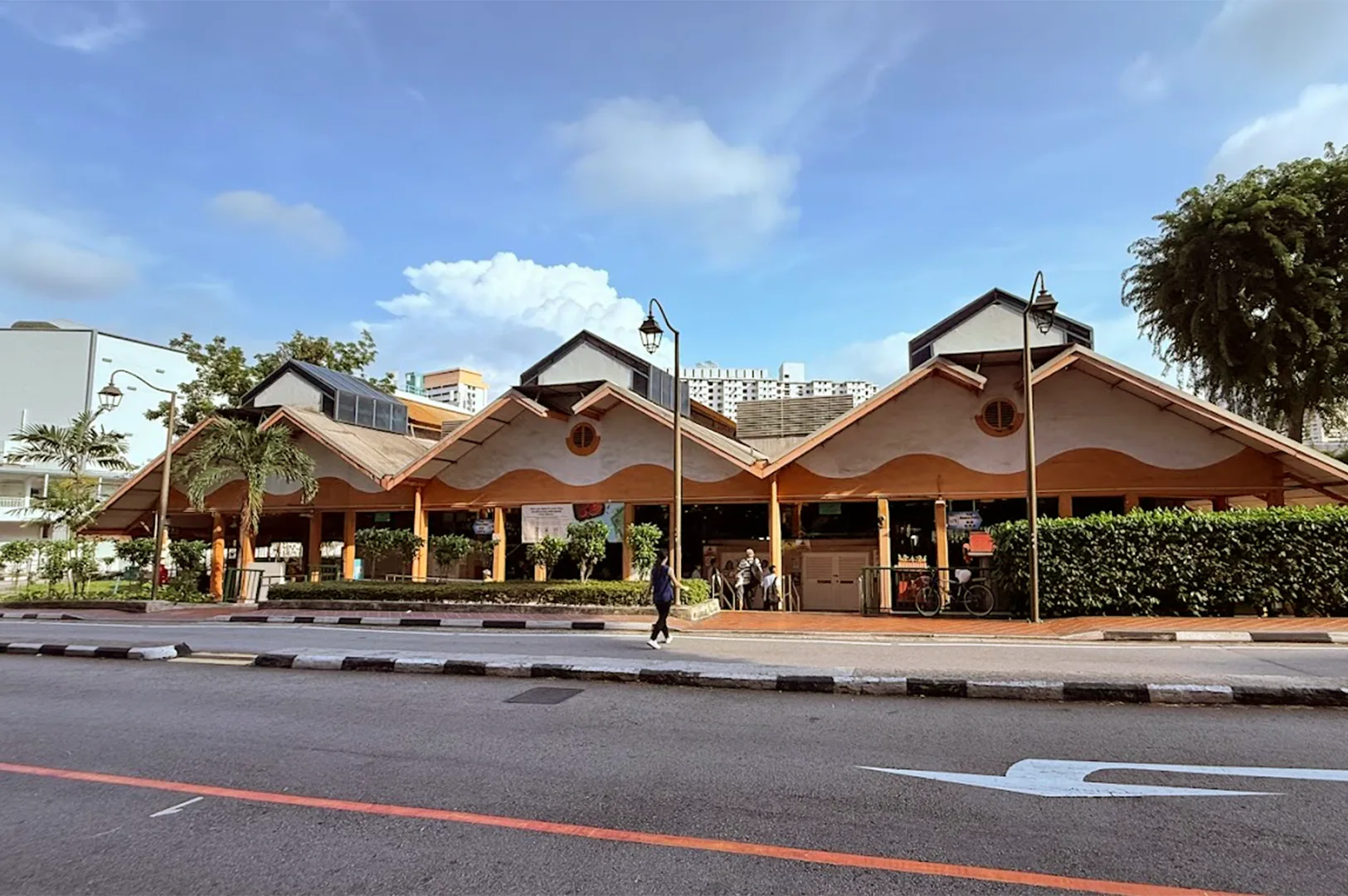 The exterior view of the iconic Maxwell Food Centre in Singapore on opening hours near maxwell mrt station, showcasing its distinctive orange-hued architecture and roof structure near the street.