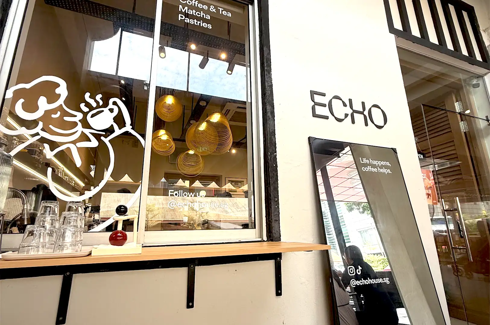 The exterior storefront of Echo Cafe at KADA, Singapore, featuring modern minimalist signage, a window display of hanging golden lights, and the encouraging slogan.