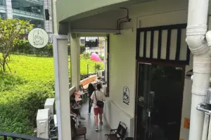 Exterior view of the entrance to Kyuukei Coffee near Maxwell, Singapore, featuring an outdoor seating area and a unique cat-themed logo sign, creating an inviting, cosy coffee shop atmosphere.