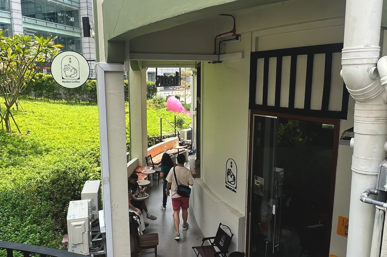 Exterior view of the entrance to Kyuukei Coffee near Maxwell, Singapore, featuring an outdoor seating area and a unique cat-themed logo sign, creating an inviting, cosy coffee shop atmosphere.