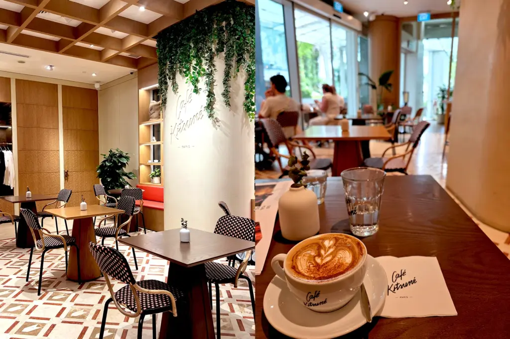 Split image of a warm interior of Café Kitsuné Singapore with modern furniture and hanging greenery, and a steaming cup of latte art coffee served on a signature branded saucer at a table inside the bright and airy Café Kitsuné at Capitol Singapore.