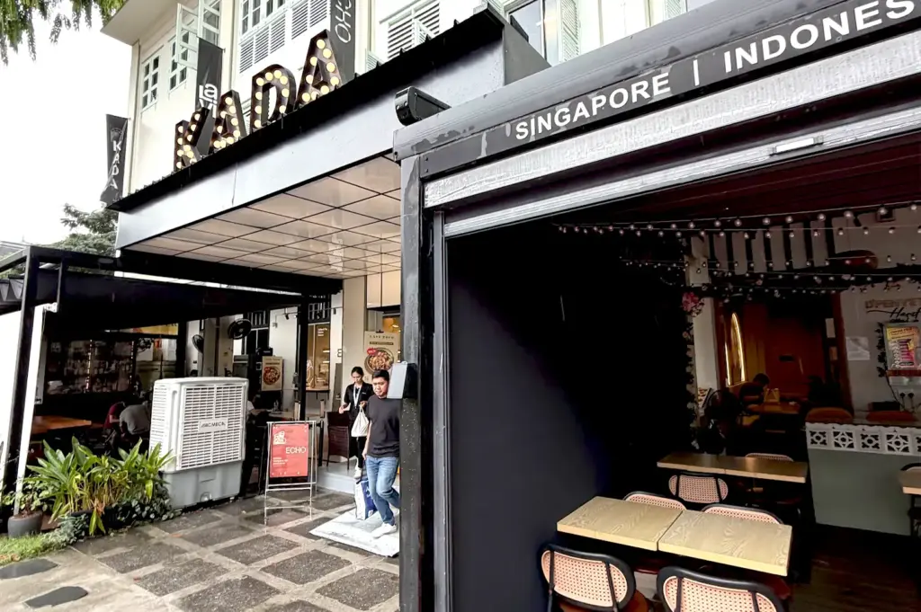 The entrance to Echo Cafe located within the KADA Singapore complex, showing its sleek, black-framed facade and adjacent outdoor seating area under a shared canopy.