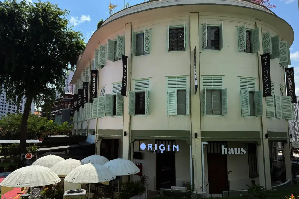 The exterior facade of the historic building housing Kyuukei Coffee and other cafes in the Maxwell district of Singapore, showing its characteristic architecture and outdoor umbrellas.