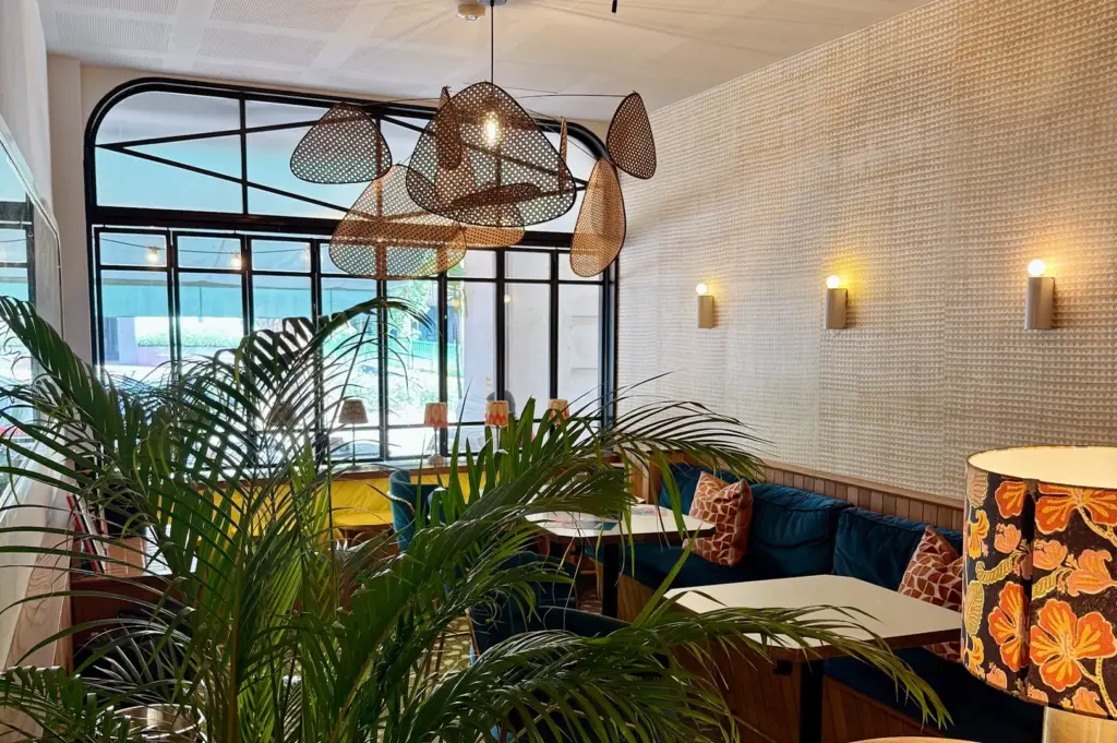 Interior of Merci Marcel showing a cozy dining nook with velvet blue booths, warm lighting, and artistic rattan pendant lamps.