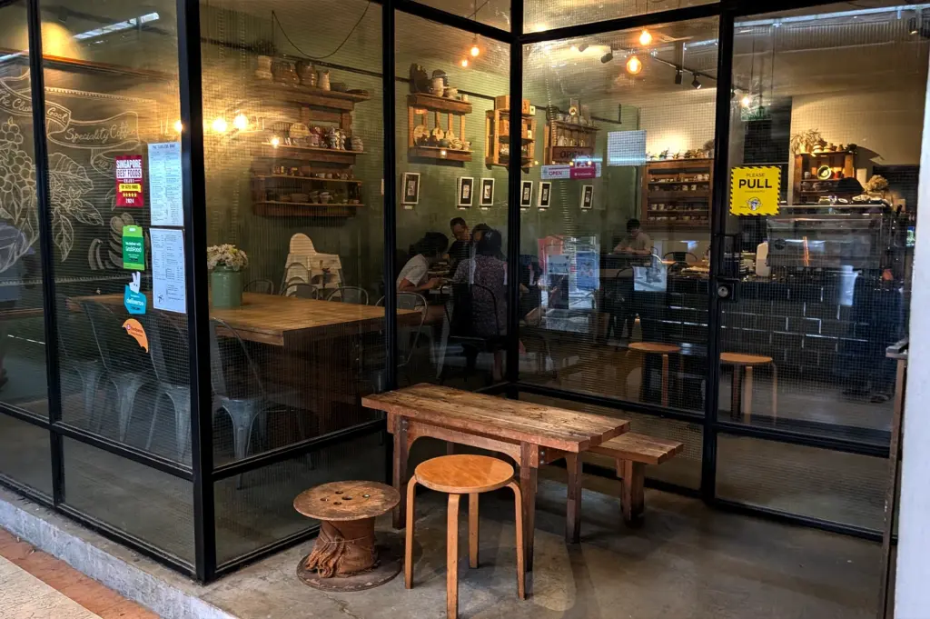 View through the glass storefront of The Clueless Goat in Singapore, highlighting its cozy, rustic interior and comfortable seating area.