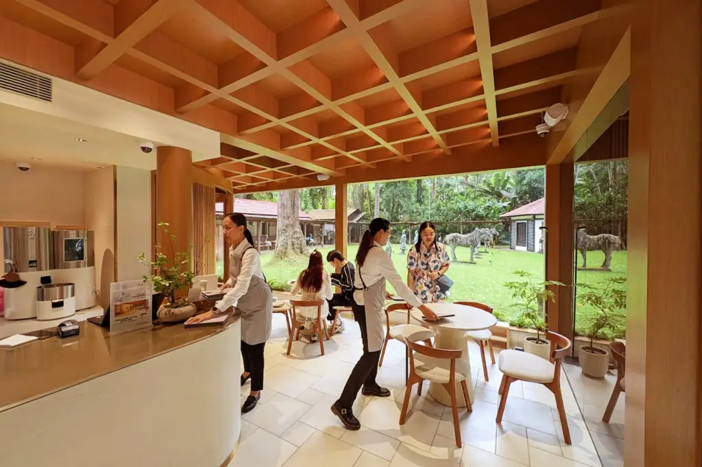 Interior view of Ami Patisserie in Singapore, highlighting elegant, warm wooden decor and large glass windows overlooking a serene garden lawn with animal sculptures.