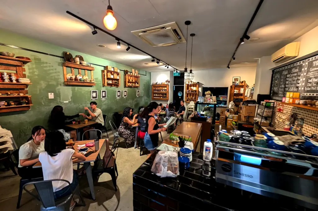 Inside The Clueless Goat Singapore, showing the warm, inviting atmosphere, green feature wall with rustic decor, and customers enjoying brunch.