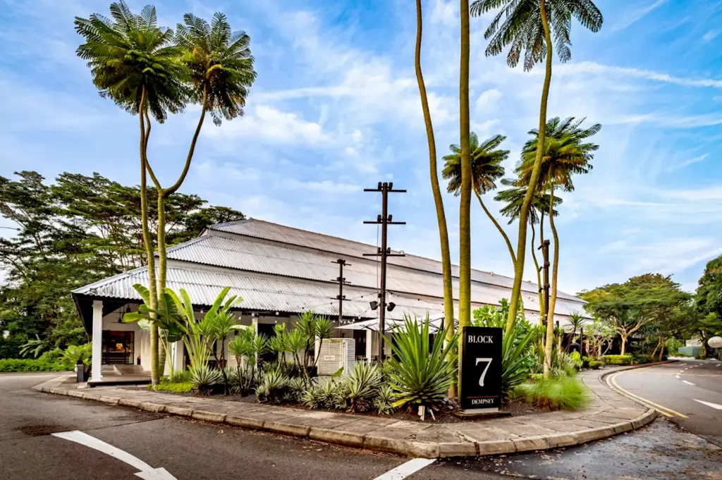 Exterior shot of Burnt Ends Bakery located at Block 7 Dempsey, surrounded by lush tropical greenery and tall palm trees under a bright blue sky.